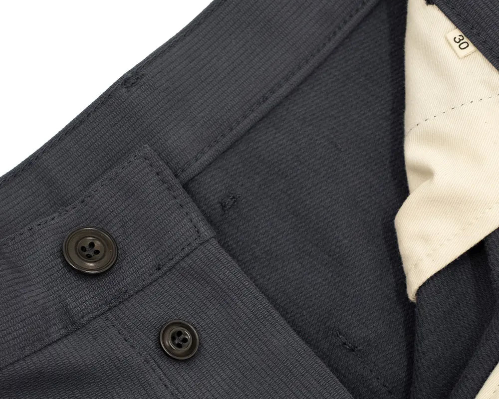 Close-up detail of a dark navy woven fabric garment, showing a buttoned pocket flap, dark buttons, and a cream-colored inner collar lining.