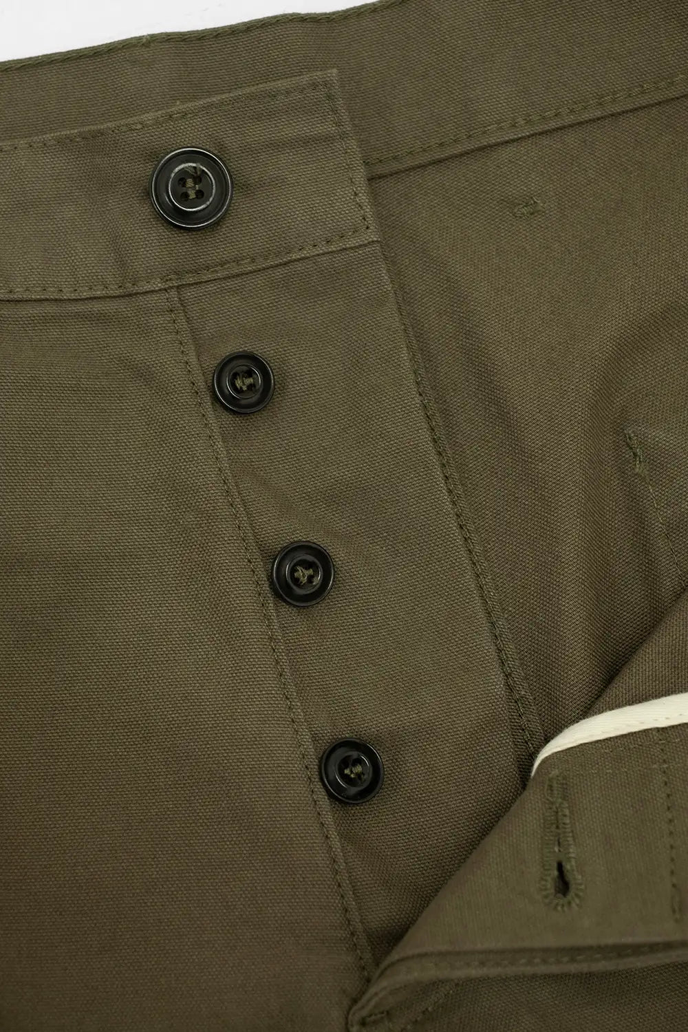 Close-up of olive green fabric with a vertical row of black buttons and a folded cuff showing a white inner lining.