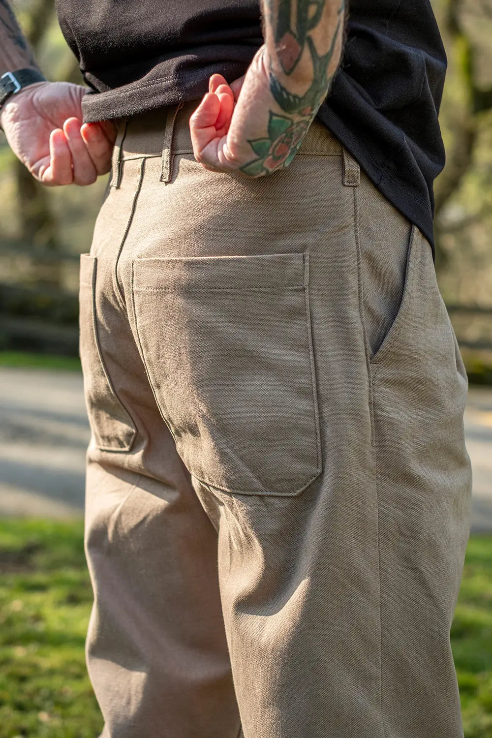 Close-up of a person wearing beige cargo-style pants with a black shirt, standing outdoors in a park-like setting.