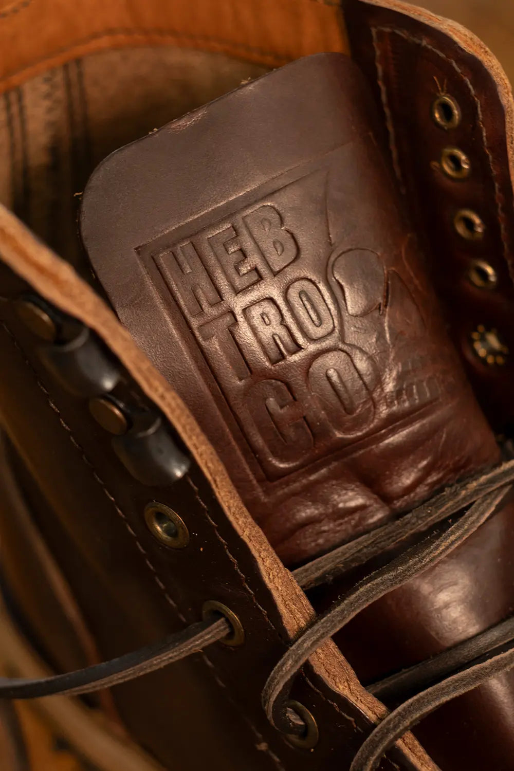 Close-up of a dark brown leather lace-up boot with a prominent embossed 'HEB TRO CO' logo on the tongue lining.