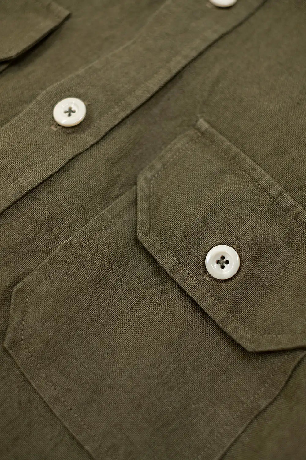 Close-up of an olive green linen shirt with white buttons and a chest pocket.