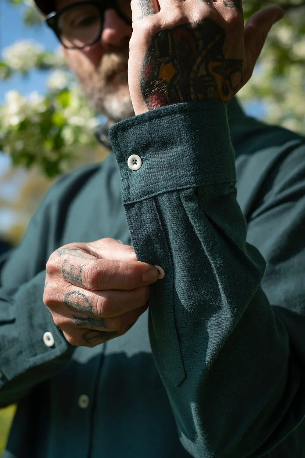 A close-up of a man outdoors wearing a dark green long-sleeve button-up shirt, showing the fabric texture and buttoned cuff.