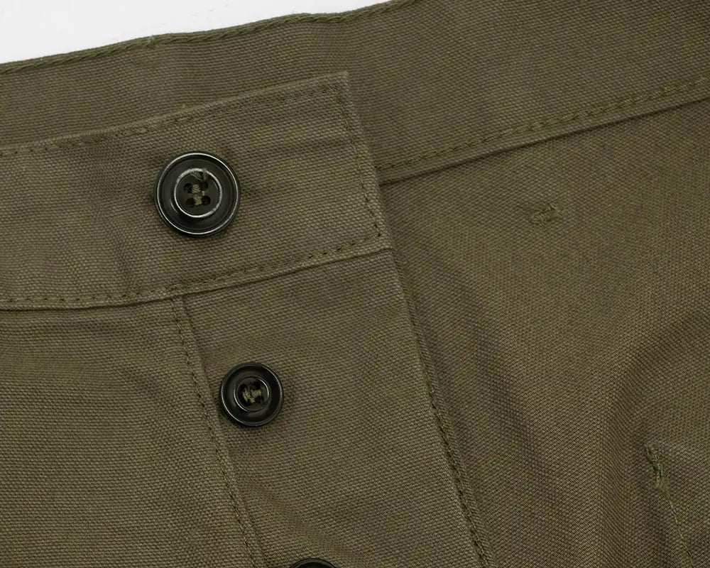 Close-up detail of olive green canvas pants showing a buttoned pocket and black buttons.