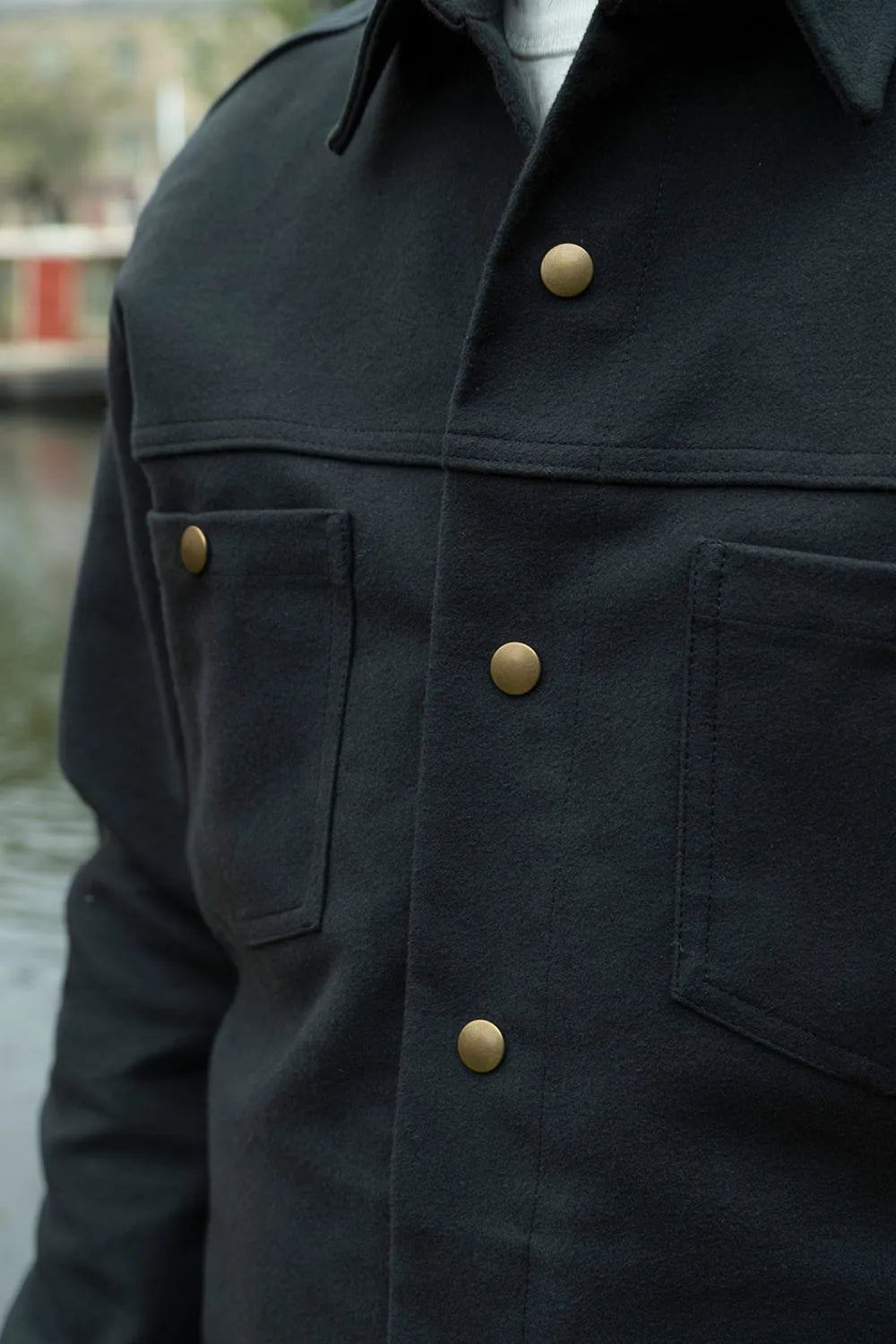 Close-up of a gray moleskin ironshirt with brass buttons, worn by a person outdoors near water.