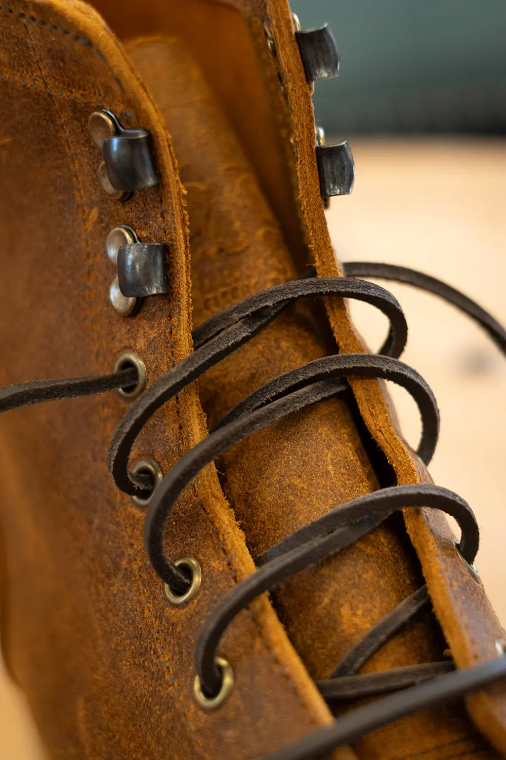 Close-up of a brown leather lace-up boot with dark brown laces threaded through metal eyelets.
