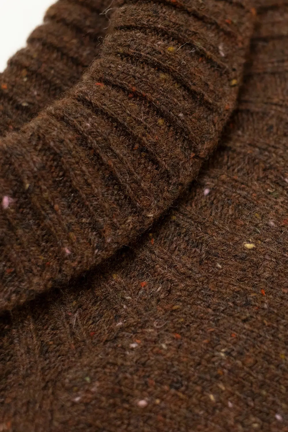 Close-up of a dark brown ribbed knit fabric with flecks of multicolored yarn, showing the texture and weave detail.