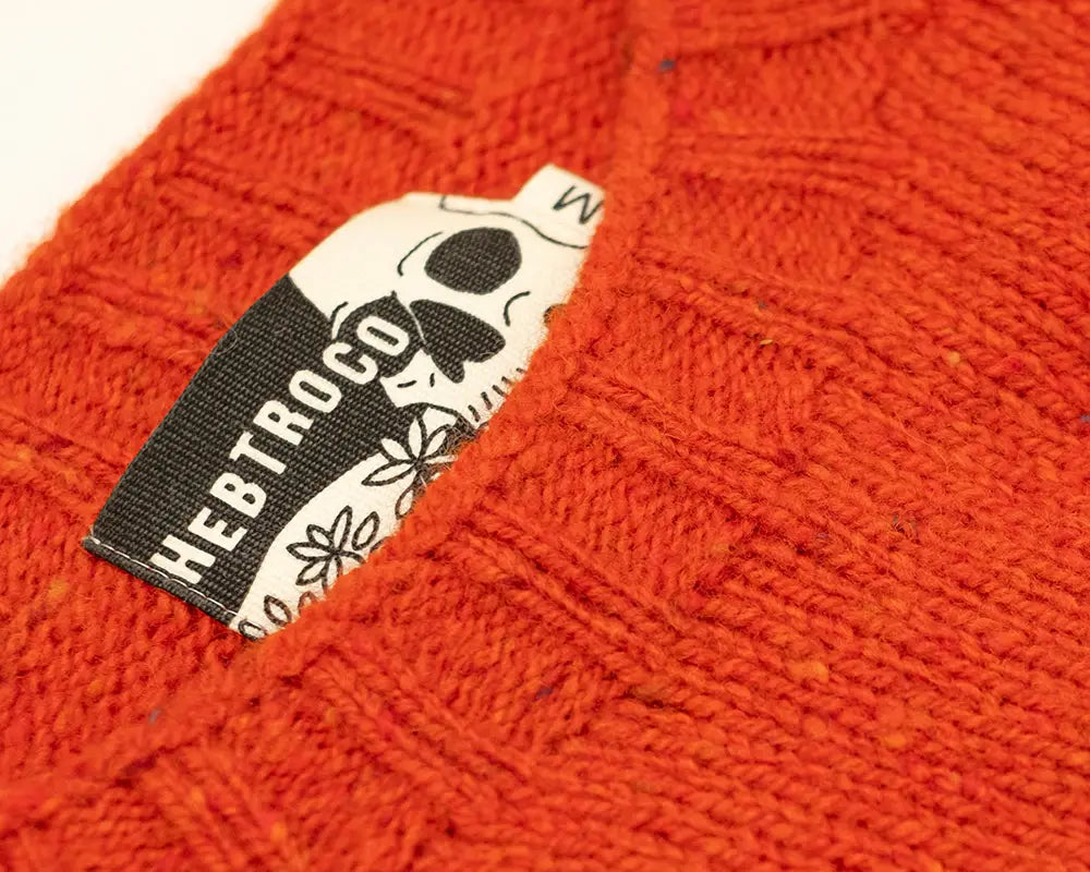Close-up of a textured orange knit beanie with a black and white HEBTROCO brand tag sewn inside the cuff.