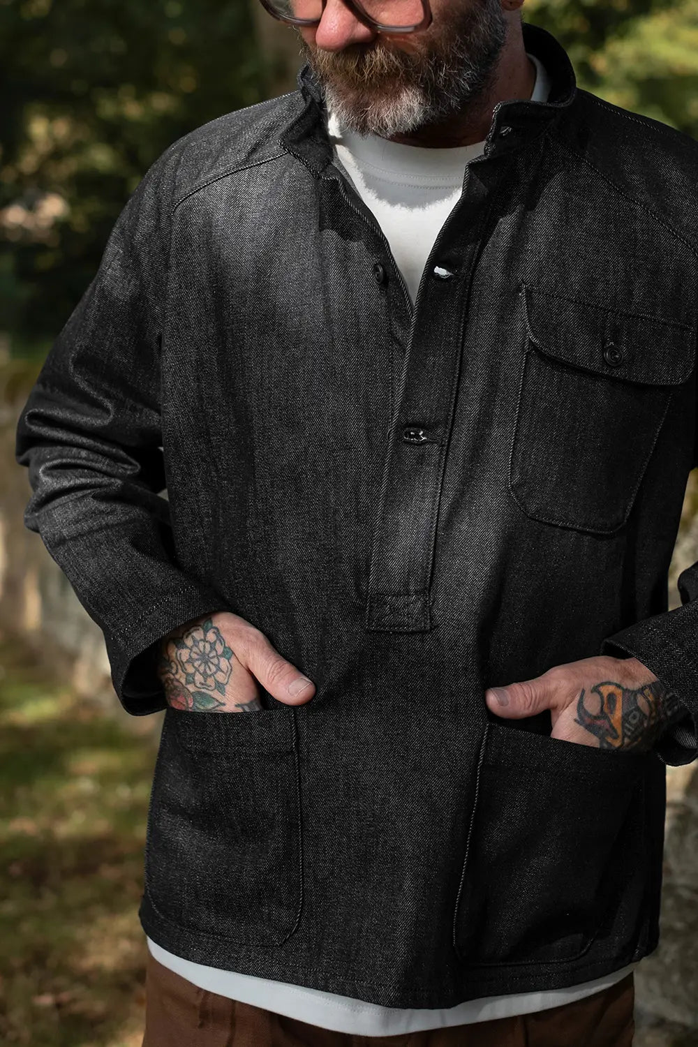 A man wearing a dark charcoal gray long-sleeve button-up shirt jacket with a chest pocket, shown outdoors with his hands in the front pockets.