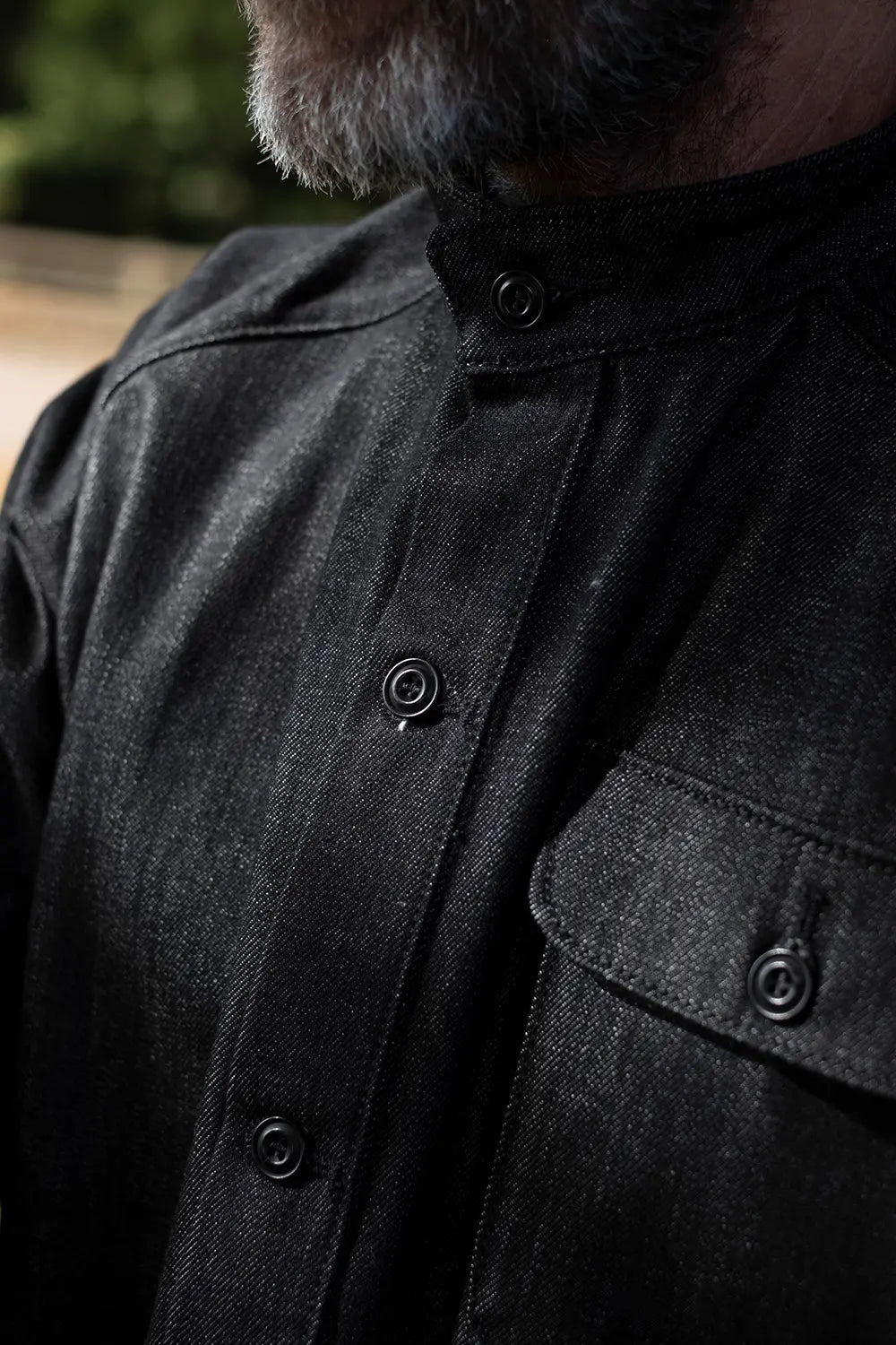 Close-up of a person wearing a dark charcoal gray textured button-up shirt with a stand collar and a chest pocket.