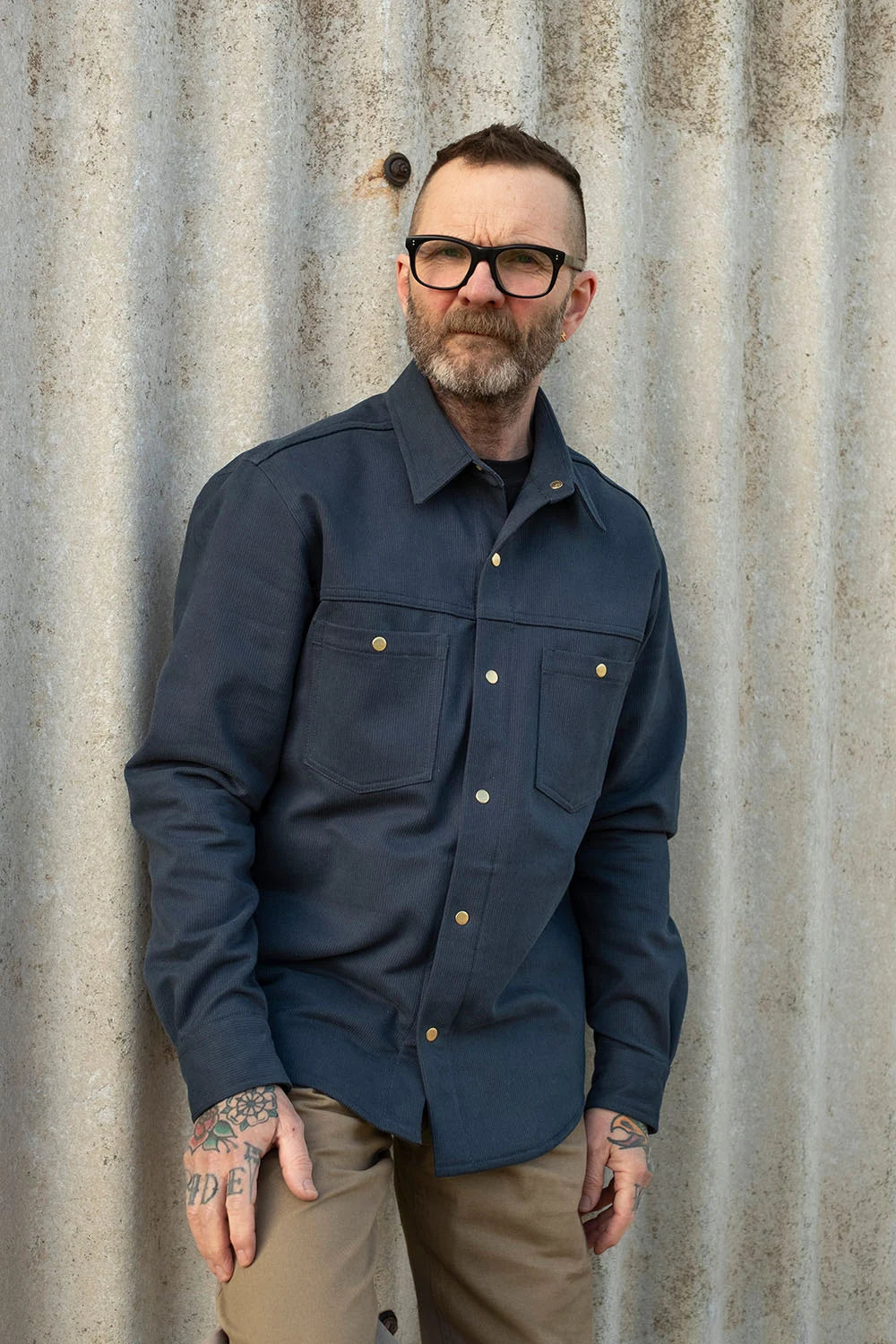 Man wearing a bedford cord navy iron shirt against a corrugated metal background