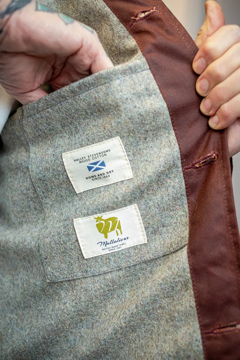 Close-up of wool interior of the rascal vest with a hand holding the flap, showing a gray wool body, brown lining, and two brand labels: Mullion and Spinning Kyt Wools.