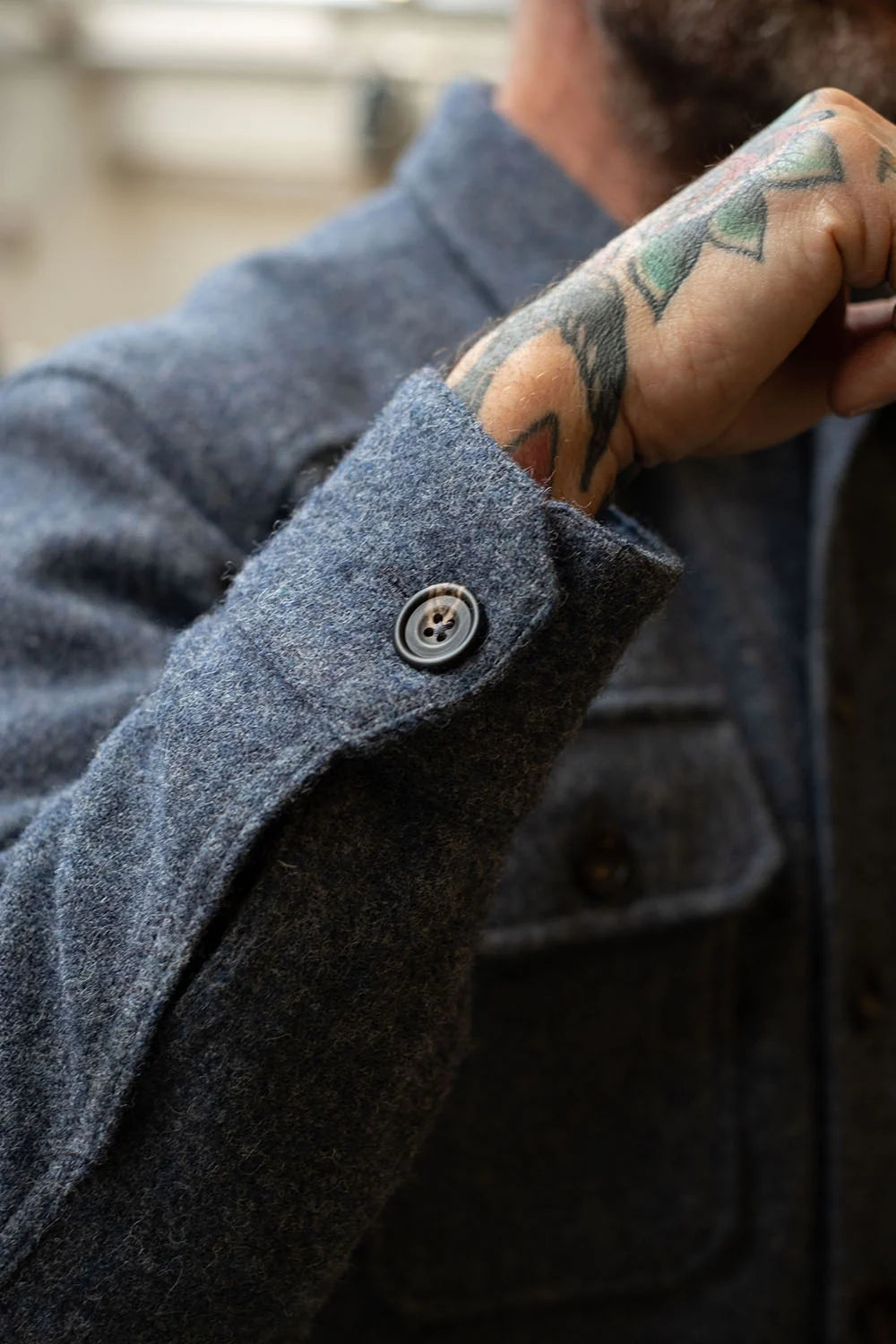 Close-up of a person wearing a dark charcoal gray wool-blend jacket, showing the buttoned cuff and part of the tattooed hand.